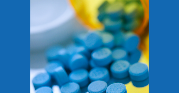 Many blue medicinal tablets spill out of an orange prescription bottle