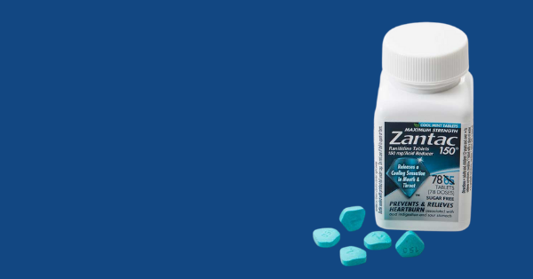 Against a blue background, a bottle of ZANTAC and several blue-green pills spilled out