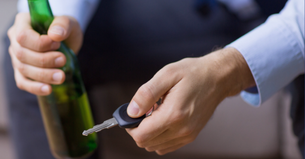 A man's hands hold a green beer bottle and car keys