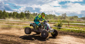 A person in a green suit and helmet rides an ATV down a dirt trail