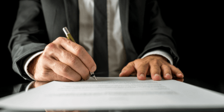 The hands and torso of a man in a suit signing a paper